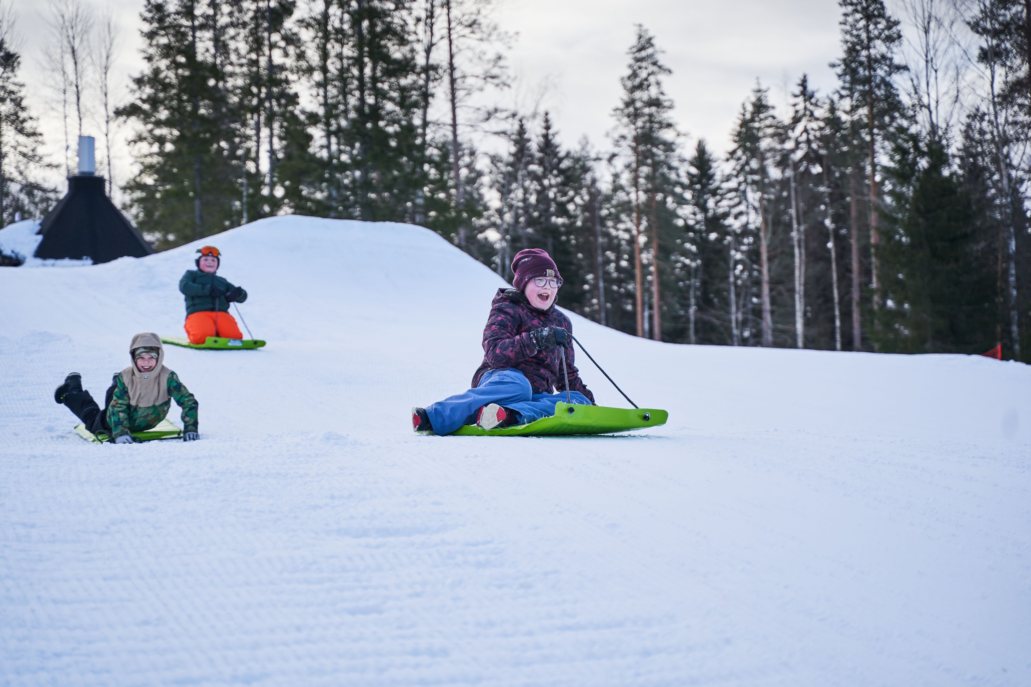 kolma laskijaa pulkkamäessä, taustalla luminen metsä