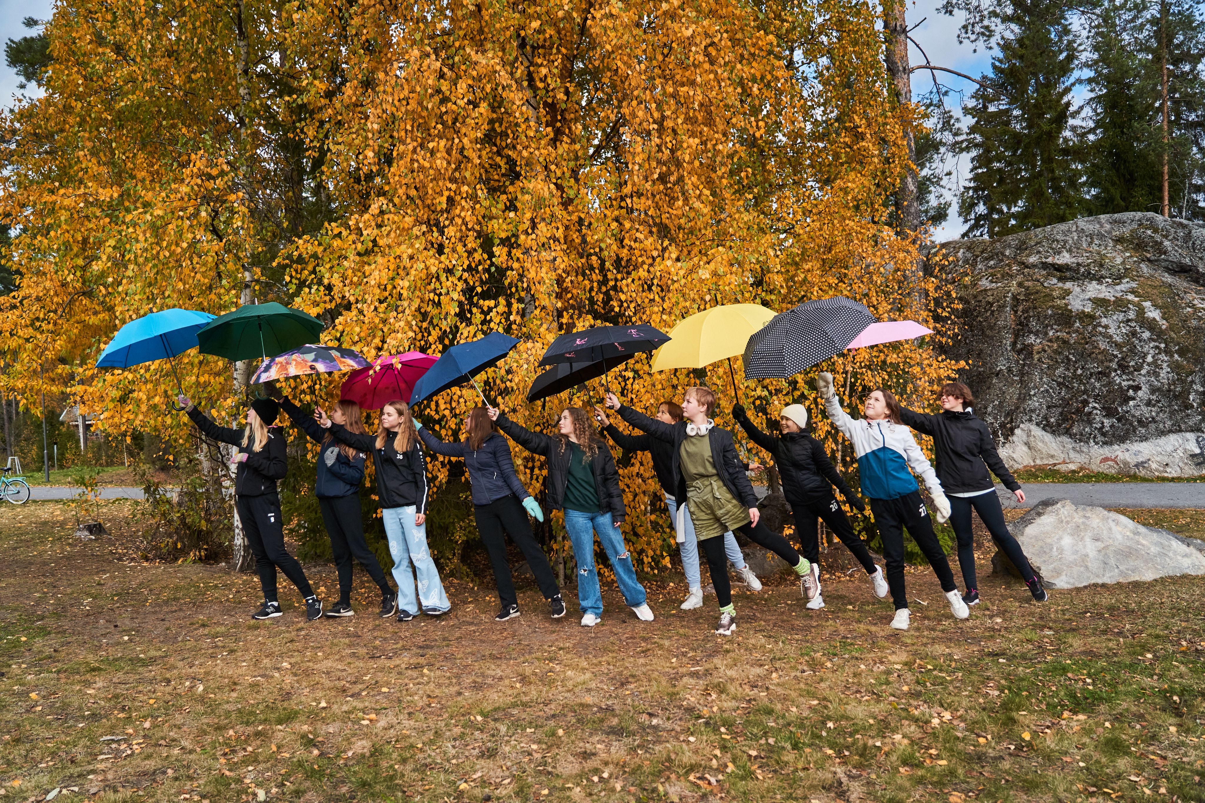 Nuoret sateenvarjon alla ruskametsän edessä