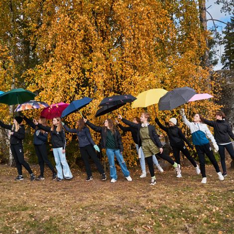 Nuoret sateenvarjon alla ruskametsän edessä